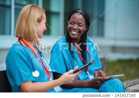 Diverse nurses collaborating outdoors using digital tablets Diverse nurses collaborating outdoors using digital tablets 141917193