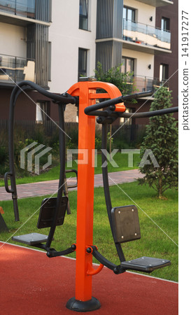 Outdoor fitness gym equipment with vibrant orange accents in a modern apartment complex park area Outdoor fitness gym equipment with vibrant orange accents in a modern apartment complex park area 141917277