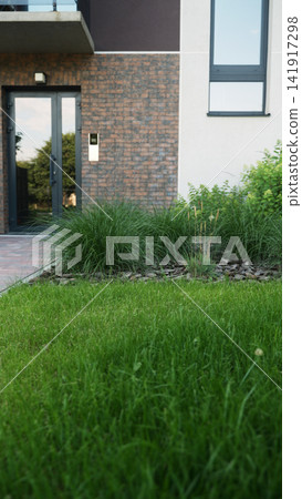 Modern building exterior showcasing green lawn, decorative plants, brick facade, and front entrance reflecting surrounding nature Modern building exterior showcasing green lawn, decorative plants, brick facade, and front entrance reflecting surrounding nature 141917298