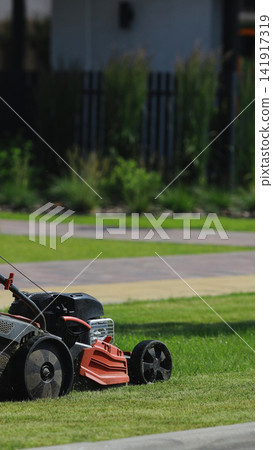 Lawn mower cutting fresh green grass on a sunny day, creating neat turf in a modern home garden Lawn mower cutting fresh green grass on a sunny day, creating neat turf in a modern home garden 141917319