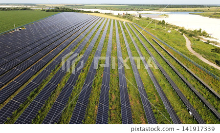 Solar farm generating clean energy with rows of photovoltaic panels on green field near lake and forest Solar farm generating clean energy with rows of photovoltaic panels on green field near lake and forest 141917339