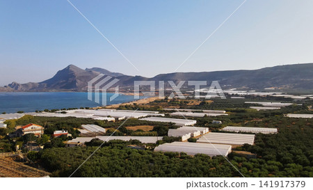 Extensive agricultural greenhouses and olive groves lining Falassarna beach with mountains and Mediterranean sea Extensive agricultural greenhouses and olive groves lining Falassarna beach with mountains and Mediterranean sea 141917379
