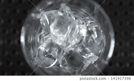 Ice cubes filling a glass with refreshing coldness, preparing a cool drink on a bar mat, top view macro detail Ice cubes filling a glass with refreshing coldness, preparing a cool drink on a bar mat, top view macro detail 141917390