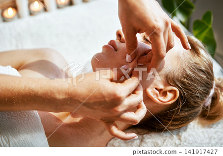 Candlelit Spa Facial Treatment Therapist Fingers Pressing Cheek and Temple of Relaxed Woman on White Towel in Warm Amber Light Candlelit Spa Facial Treatment Therapist Fingers Pressing Cheek and Temple of Relaxed Woman on White Towel in Warm Amber Light 141917427