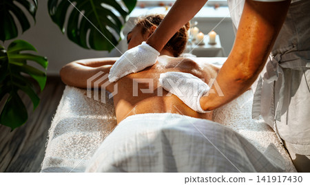 Mitt Exfoliation Back Treatment at Biophilic Day Spa Therapist Using White Massage Mitts on Womans Back Near Candles and Monstera Plant Mitt Exfoliation Back Treatment at Biophilic Day Spa Therapist Using White Massage Mitts on Womans Back Near Candles and Monstera Plant 141917430