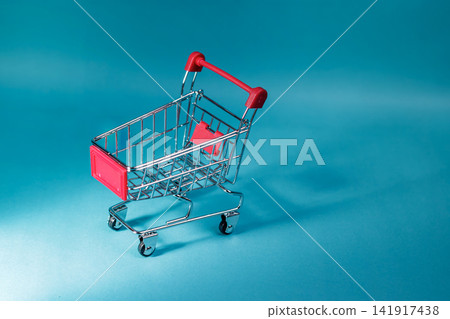An empty small metal shopping cart with red handles set against a blue gradient background for commerce and sale layouts. High Quality Photo An empty small metal shopping cart with red handles set against a blue gradient background for commerce and sale layouts. High Quality Photo 141917438