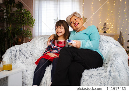 Grandmother granddaughter watching TV together laughing on sofa 141917483
