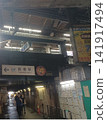 Coin lockers are located on the right side of the low-ceilinged, dark, and old corridor, with a train station platform overhead. 141917494