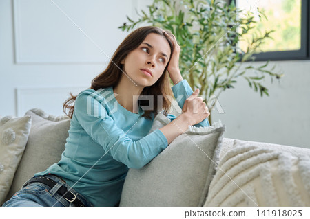Pensive teen student girl sitting thoughtful on sofa leaning hand Pensive teen student girl sitting thoughtful on sofa leaning hand 141918025
