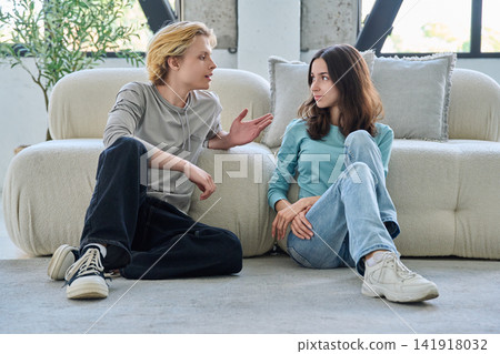 Young student friends sitting on living room floor having conversation Young student friends sitting on living room floor having conversation 141918032