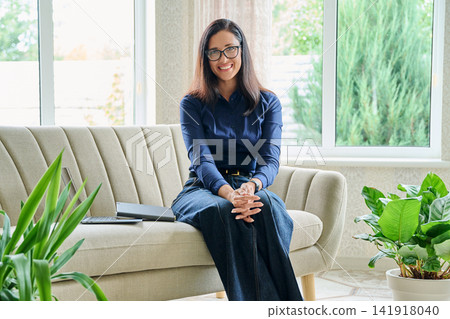 Happy smiling businesswoman leaning on sofa looking at camera in modern cozy home office Happy smiling businesswoman leaning on sofa looking at camera in modern cozy home office 141918040
