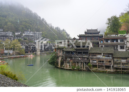 Medieval wooden buildings on Tuojiang River, boats and mountains in morning in Fenghuang, China Medieval wooden buildings on Tuojiang River, boats and mountains in morning in Fenghuang, China 141918065