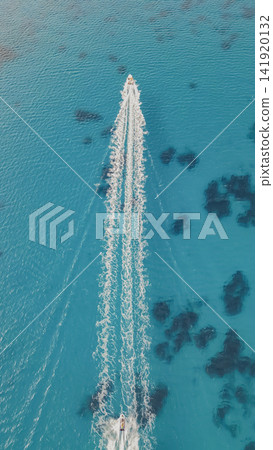 Vertical drone top down view of motorboat and jet ski speeding through clear turquoise sea water leaving white foam trail on sunny summer day stock photo Vertical drone top down view of motorboat and jet ski speeding through clear turquoise sea water leaving white foam trail on sunny summer day stock photo 141920132