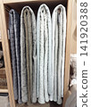 Four different quilted blankets hang vertically in a light wood shelf in a store. They go from dark grey on the left to off-white on the right, showing various textures and stitching patterns. 141920388