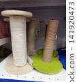 Close-up of cat scratching posts on a store shelf. Two main types are visible: one with plain wooden bases and white rope wrapping, and another with green fuzzy bases and brown sisal rope wrapping. 141920473