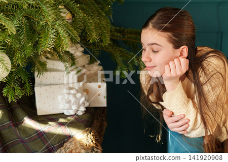 Teen girl relaxing by Christmas tree and wrapped holiday gifts Teen girl relaxing by Christmas tree and wrapped holiday gifts 141920908