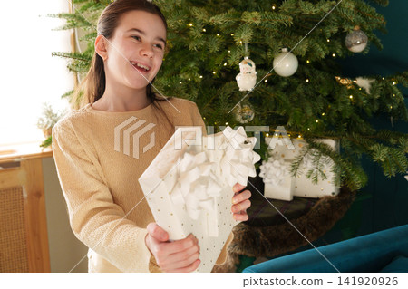 Teen girl offering wrapped Christmas gifts with festive smile Teen girl offering wrapped Christmas gifts with festive smile 141920926