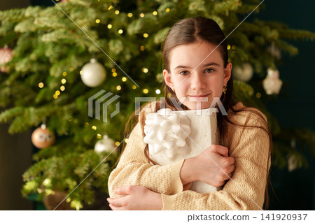 Teen girl hugging wrapped Christmas gifts and looking at camera Teen girl hugging wrapped Christmas gifts and looking at camera 141920937