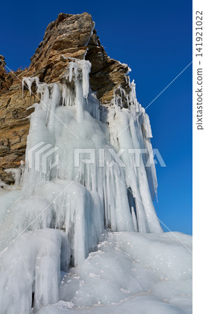 Ice formations covering rocky cliffs against a blue sky: Lake Baikal in winter. Ice formations covering rocky cliffs against a blue sky: Lake Baikal in winter. 141921022