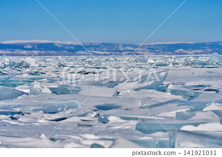 Lake Baikal and snow-capped mountains in winter, with shattered blue ice sheets stretching across the landscape. Lake Baikal and snow-capped mountains in winter, with shattered blue ice sheets stretching across the landscape. 141921031