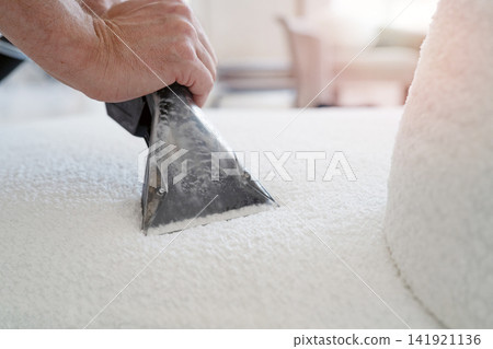 Close-up of worker hands using a professional extraction vacuum tool to clean a white sofa. Close-up of worker hands using a professional extraction vacuum tool to clean a white sofa. 141921136