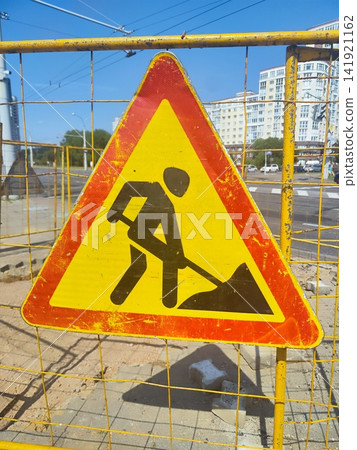 Triangular road work sign with a red border and yellow interior featuring a black silhouette of a person digging with a shovel Triangular road work sign with a red border and yellow interior featuring a black silhouette of a person digging with a shovel 141921162