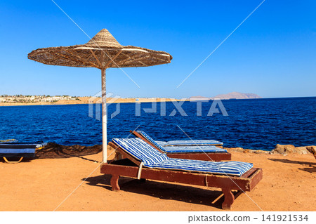 Sun umbrellas and chaise lounges on tropical beach. Concept of rest, relaxation, holidays, resort Sun umbrellas and chaise lounges on tropical beach. Concept of rest, relaxation, holidays, resort 141921534