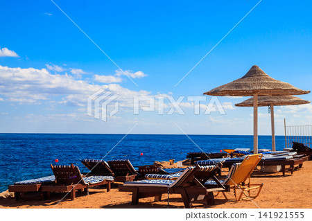 Sun umbrellas and chaise lounges on tropical beach. Concept of rest, relaxation, holidays, resort Sun umbrellas and chaise lounges on tropical beach. Concept of rest, relaxation, holidays, resort 141921555