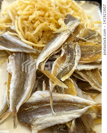 Many different dried fish snacks on grey table Dried salted fish as snacks or jerky, seafood as slices. Dried seafood snacks as a background for your design 141921607
