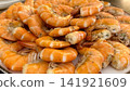 A plate of shrimp is on a table with other plates of food. The shrimp are cooked and arranged in a neat pile 141921609