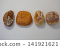 Four varieties of freshly baked bread on white table including round oval long and dark artisan loaves 141921621