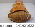 Four varieties of freshly baked bread on white table including round oval long and dark artisan loaves 141921622