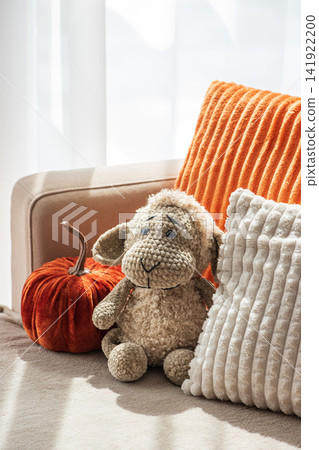 Cozy autumnal interior scene featuring plush stuffed sheep toy and decorative velvet pumpkin beside soft textured cushions for festive home decor Cozy autumnal interior scene featuring plush stuffed sheep toy and decorative velvet pumpkin beside soft textured cushions for festive home decor 141922200
