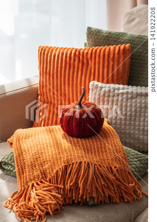 Cozy autumn living room arrangement with plush pillows and decorative pumpkin creating warm inviting home atmosphere Cozy autumn living room arrangement with plush pillows and decorative pumpkin creating warm inviting home atmosphere 141922208