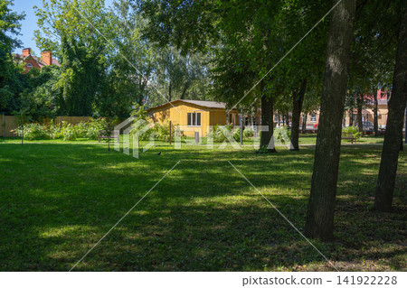View of a fresh green grass meadow in a shaded summer park with bright sunlight and distant building. Perfect stock image for ecology campaigns, city parks, landscape design, and summer lifestyle View of a fresh green grass meadow in a shaded summer park with bright sunlight and distant building. Perfect stock image for ecology campaigns, city parks, landscape design, and summer lifestyle 141922228