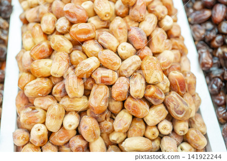 Top view close-up texture of dried sweet dates displayed at an eastern food market stall. Ideal background stock photo for healthy snacks, vegan diet, dried fruits, and middle eastern food topics Top view close-up texture of dried sweet dates displayed at an eastern food market stall. Ideal background stock photo for healthy snacks, vegan diet, dried fruits, and middle eastern food topics 141922244
