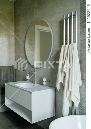 White suspended sink cabinet with round mirror and modern chrome ladder towel dryer hanging in a tiled bathroom. Perfect visual for interior design, sanitaryware, and plumbing accessories White suspended sink cabinet with round mirror and modern chrome ladder towel dryer hanging in a tiled bathroom. Perfect visual for interior design, sanitaryware, and plumbing accessories 141922446
