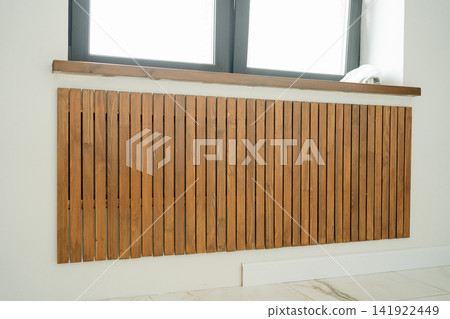 Close-up of vertical wooden slats masking a radiator system under a window. Great visual asset for interior architecture, carpentry design, heating equipment covers, and home decor stock Close-up of vertical wooden slats masking a radiator system under a window. Great visual asset for interior architecture, carpentry design, heating equipment covers, and home decor stock 141922449