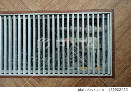 Built-in floor radiator with exposed interior valves and metal protective screen on a wooden floor. Perfect stock image for building construction, heating maintenance, and home repair Built-in floor radiator with exposed interior valves and metal protective screen on a wooden floor. Perfect stock image for building construction, heating maintenance, and home repair 141922453