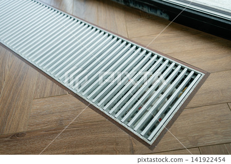 Sleek metal trench radiator in herringbone wood floor providing invisible thermal barrier near glass doors. Great image for heating system design, smart homes, and modern living spaces Sleek metal trench radiator in herringbone wood floor providing invisible thermal barrier near glass doors. Great image for heating system design, smart homes, and modern living spaces 141922454