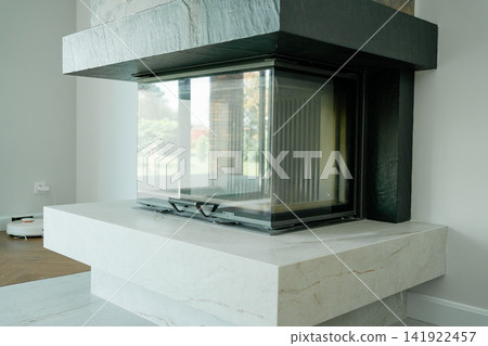 Minimalist corner closed fireplace built with stone and dark chimney hood in a bright house interior. Perfect stock photo for home warmth, interior architecture, heating solutions, and decor. Minimalist corner closed fireplace built with stone and dark chimney hood in a bright house interior. Perfect stock photo for home warmth, interior architecture, heating solutions, and decor. 141922457