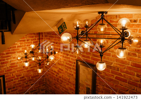 Stylish geometric pendant lights glowing above a wooden staircase with brick wall. Perfect stock image for modern cafe interiors, industrial style lighting, atmosphere, and home renovation Stylish geometric pendant lights glowing above a wooden staircase with brick wall. Perfect stock image for modern cafe interiors, industrial style lighting, atmosphere, and home renovation 141922473