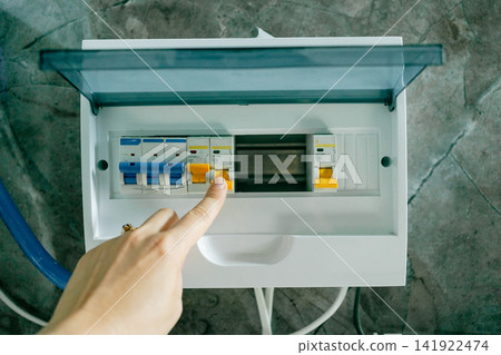 Close-up view of a person operating a breaker switch in an electrical control panel. Perfect stock image for electrician work, power grid management, home repair, and energy concepts Close-up view of a person operating a breaker switch in an electrical control panel. Perfect stock image for electrician work, power grid management, home repair, and energy concepts 141922474