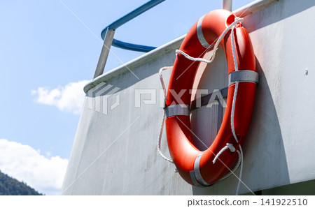 Bright orange lifebuoy on board a boat, representing water transport and the boating setting in a clean maritime environment. Bright orange lifebuoy on board a boat, representing water transport and the boating setting in a clean maritime environment. 141922510