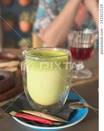 Matcha Latte in Double Wall Glass. Creamy green matcha latte served in transparent double wall glass at cafe table. Modern drink scene, wellness, tea culture, healthy lifestyle, relaxing coffee shop Matcha Latte in Double Wall Glass. Creamy green matcha latte served in transparent double wall glass at cafe table. Modern drink scene, wellness, tea culture, healthy lifestyle, relaxing coffee shop 141922529