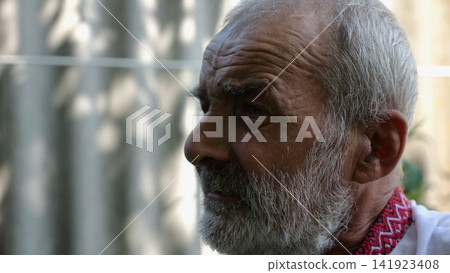 Profile of senior despair ukrainian man at summer garden. Elderly sad bearded male wearing an embroidered shirt looking into camera outdoor. Mature human in vyshyvanka with upset emotions 141923408