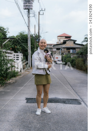 Smiling bald woman holding chihuahua dog on city street Smiling bald woman holding chihuahua dog on city street 141924390