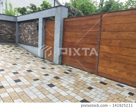 Modern House Exterior with Wooden Gate Brick Wall and Paved Driveway Modern House Exterior with Wooden Gate Brick Wall and Paved Driveway 141925211