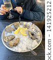 Fresh Oysters on Ice with Lemon Wedges and Glass of White Wine in Restaurant 141925212