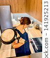 Woman Holding Frying Pan While Turning on Electric Stove Top in Modern Kitchen 141925213